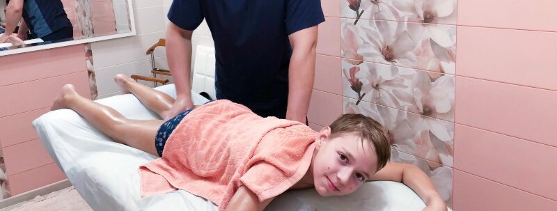 Массажист в массажном салоне делает детский массаж ребенку